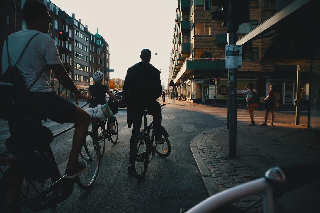 Affärsmänniskor i professionell klädsel cyklar genom en stadsgata i skymningen.